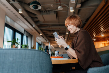 Mature female checking messages while seated at shared workspace