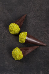 Dubai chocolate dessert. Dark chocolate cone with a ball of crispy kataifi dough with pistachio paste. Dark gray background. Top view	