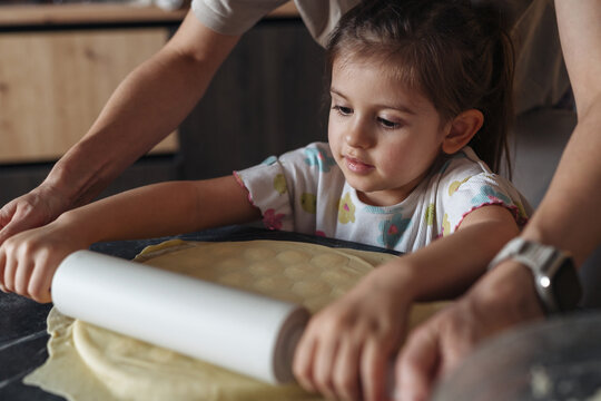Young girl patiently practicing dough rolling under watchful guidance