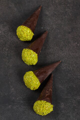 Vegan Dubai chocolate dessert. Dark chocolate cone with a ball of crispy kataifi dough with pistachio paste. Dark gray background. Top view	