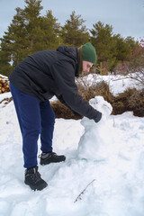 Man building a snowman in winter landscape outdoors