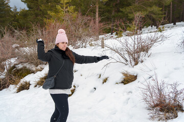 Woman wearing pink beanie throwing snowball in winter forest