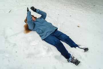 Adult woman slipping and lying on snow after winter fall outdoors