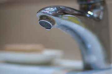 A chrome faucet with water dripping from its rusty spout. selective focus