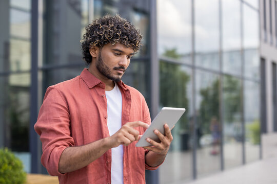 Close-up photo of a young Indian man standing outside and using a tablet