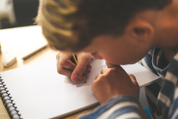 Close up view of student drawing with pencil. Boy doing homework writing on a paper. Kid hold a pencil and draw a manga at home. Teen drawing sitting at the table. Education art talent ability concept