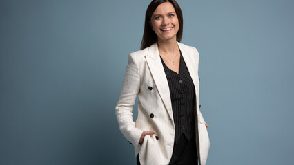 Beautiful, attractive, middle aged woman wearing casual white jacket standing isolated on blue background