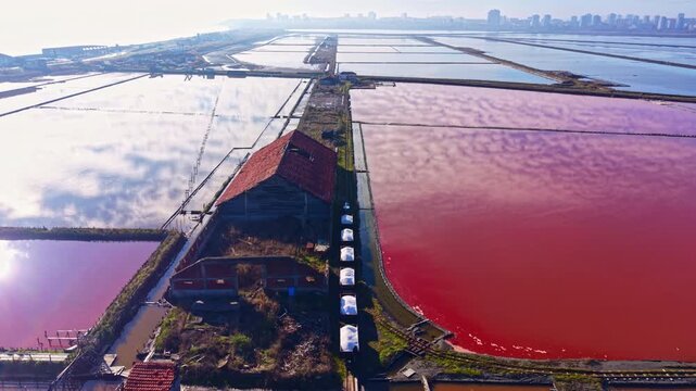 Serene salt ponds glimmer with shades of pink and blue as sunlight casts a warm glow, highlighting the solitude of an old structure amidst nature's beauty.