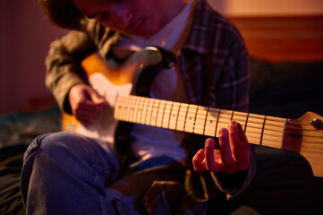 Fototapeta premium A guitarist sits indoors in warm amber light, fingers on the fretboard, enjoying a focused, intimate moment of practice and music.