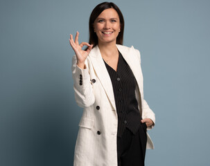 European businesswoman making an OK hand sign with confident smile against light blue background