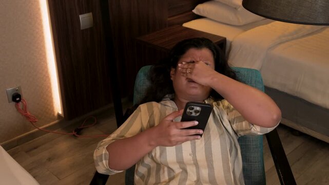 girl scrolling phone at night, she is tired and rubbing her eyes, doom scrolling concept stock video in dark background 