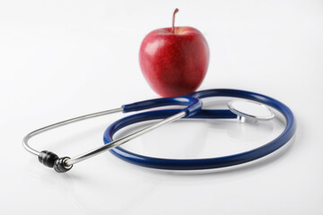 Ripe apple and stethoscope on white table, closeup