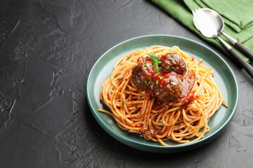Delicious pasta with meatballs served on black textured table, closeup. Space for text
