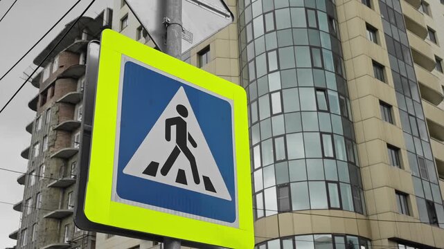Bright fluorescent pedestrian crossing sign near modern glass apartment buildings in an urban street setting, highlighting road safety, crosswalk awareness, and city infrastructure - Powered by Adobe