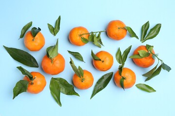 Fresh juicy tangerines and green leaves on light blue background, flat lay