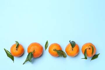 Fresh ripe tangerines and green leaves on light blue background, flat lay. Space for text
