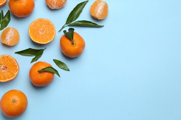 Fresh ripe tangerines and green leaves on light blue background, flat lay. Space for text