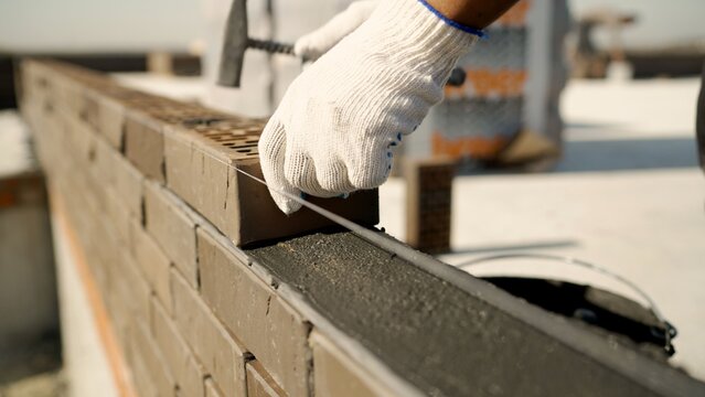 Worker laying brick wall with mortar and level string