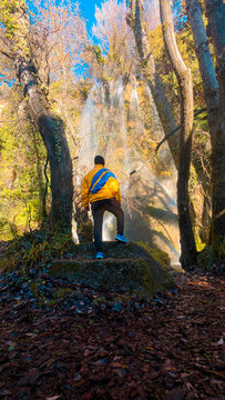 Man seen from the back, standing in front of the magnificent Fuentetoba waterfall in Soria, Spain. A tourist enjoying the breathtaking scenery during a winter hiking adventure in nature.