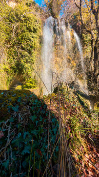 Vertical shot of the stunning Fuentetoba waterfall, a natural monument in Soria, Spain. The powerful water flows over ancient mossy rocks, creating a scene of pure natural beauty.