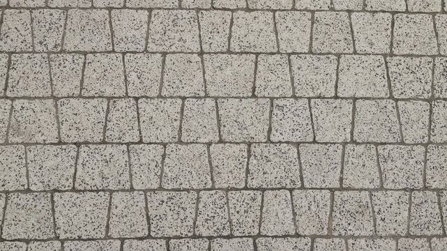 Close-up of light gray cobblestone pavement with small square stones arranged in a staggered geometric pattern, showing textured surface, grout lines, and urban walkway design