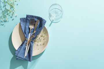 Easter table setting on blue. White plate, cutlery, easter eggs and flowers.