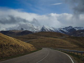Asphalt road in the Caucasus Mountains with a beautiful view against the backdrop of mountain ranges and cliffs with snow and glaciers on a cloudy, rainy day, landscape for background