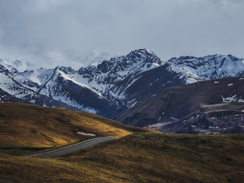 Asphalt road in the Caucasus Mountains with a beautiful view against the backdrop of mountain ranges and cliffs with snow and glaciers on a cloudy, rainy day, landscape for background