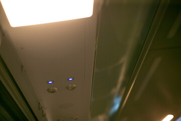 Empty commuter carriage ceiling lights glowing LED panels and ventilation vents, blue indicator LEDs, reflective metal trim, sterile calm mood, maintenance inspection atmosphere