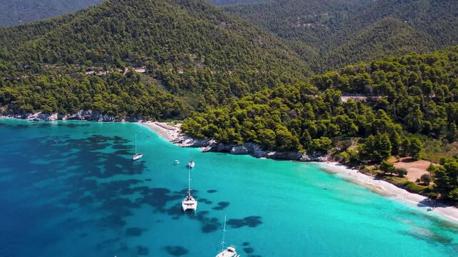Aerial view of Milia and Kastani Beach with sailboats and pine forest hills. Greece, Skopelos island . luxury summer travel and ultimate relaxation.