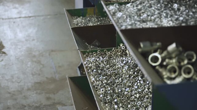 Metal nuts of different sizes are poured into different cells on factory conveyor. System for storing fasteners in factory. Shelving at workplace in machine building plant.