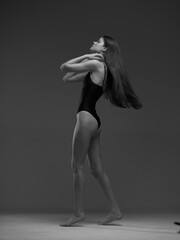 Black and white image of a graceful woman standing in a bodysuit with long flowing hair and elegant...