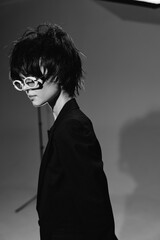 Black and white portrait of a stylish woman wearing white glasses and dark formal clothing with a contemplative expression.