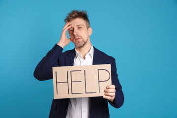 Unhappy businessman holding cardboard sign with word Help on light blue background