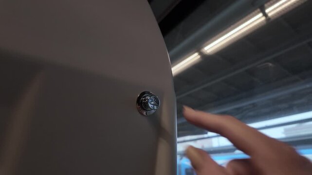 Female passenger's finger pressing a modern chrome service button inside a train carriage, symbolizing convenient public transportation and effective on-demand travel assistance