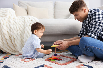 Smiling male nanny and cute little boy playing with toys on floor near sofa at home