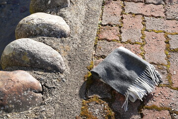 A grey and black scarf is laying on a brick walkway. The scarf is laying on the ground next to a...