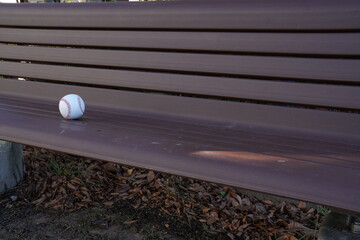 A baseball sits on a bench. The bench is made of wood and has a striped pattern. The baseball is...