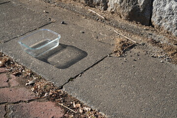 A glass bowl is sitting on a sidewalk. The bowl is empty and has a shadow on the ground. The scene is quiet and peaceful, with no other people or objects visible