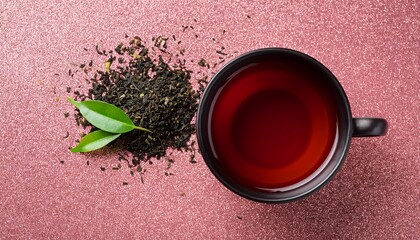top view of black cup with dark tea and loose leaf on pink glitter background