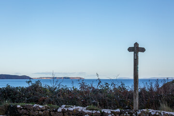 A rustic wooden directional signpost on a coastal hiking trail. This scenic view overlooks a blue sea and distant headlands under a clear sky in the British countryside.