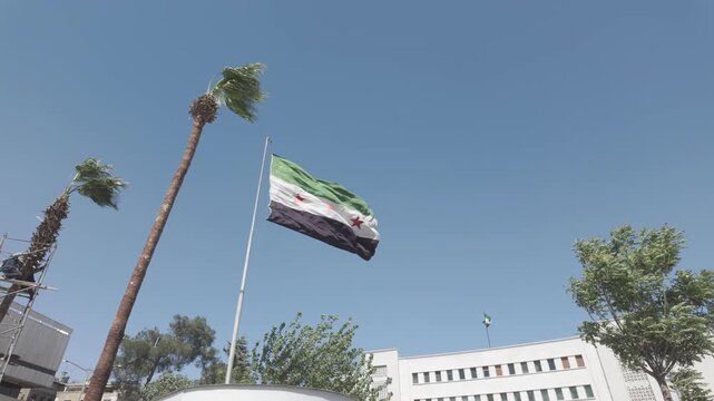 Cinematic footage of the new Syrian flag waving in the wind, displaying its bold colors and symbolic design. The scene represents identity, change, and national expression, making it suitable for news