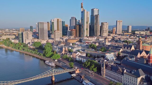 Aerial drone panning shot from Frankfurt Cathedral to the skyscraper skyline and Eiserner Steg bridge. 100m high panoramic view over the Main River and financial district in Frankfurt, Germany.