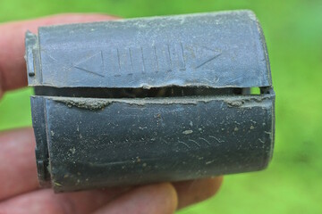 hand holding a piece of black broken plastic old pipe with a cut crack on a green background outdoors