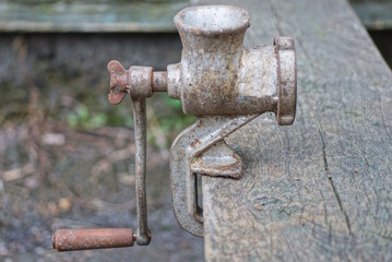 one old gray metal mechanical meat grinder stands on a wooden table in the street