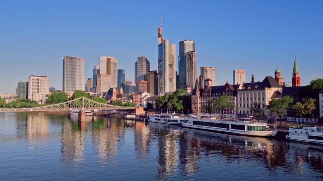 Aerial drone panning shot from Frankfurt Cathedral to the skyscraper skyline and Eiserner Steg bridge. 100m high panoramic view over the Main River and financial district in Frankfurt, Germany.