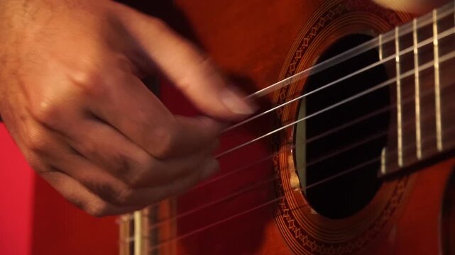 Close-up of a musician's hand plucking the strings of a classical acoustic guitar.