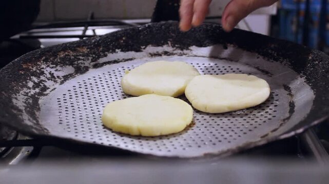 An unrecognizable woman is grilling raw cornmeal arepas in a hot pan inside her home in Neiva, Huila, Colombia. Concept of healthy food 