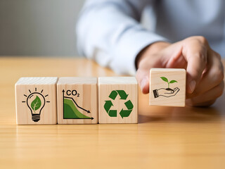 Hand arranging wooden cubes with environmental icons including light bulb leaf and recycling symbols on white background