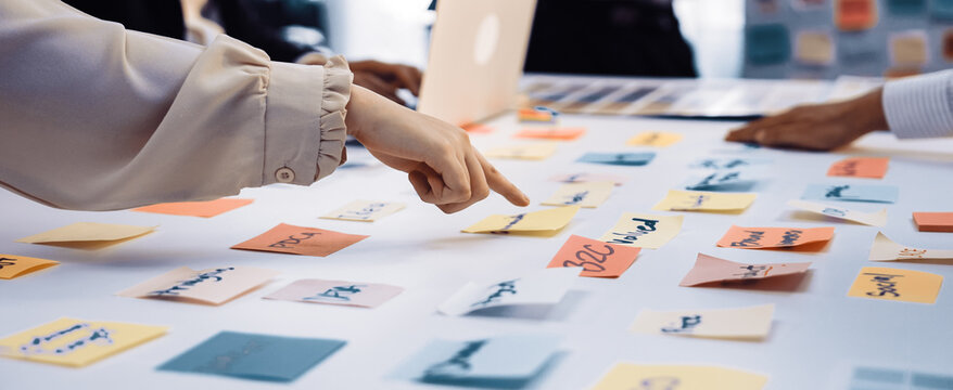 A group of professionals engages in a collaborative brainstorming session, using colorful sticky notes for idea generation and strategy planning at a modern office desk. SACTR - Powered by Adobe